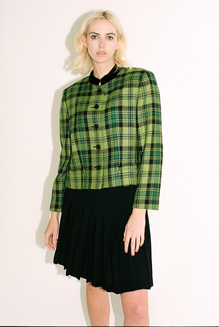 Person wearing a green plaid jacket and black skirt on a white background