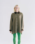 Person wearing a long brown checkered shirt with a black collar on a white background