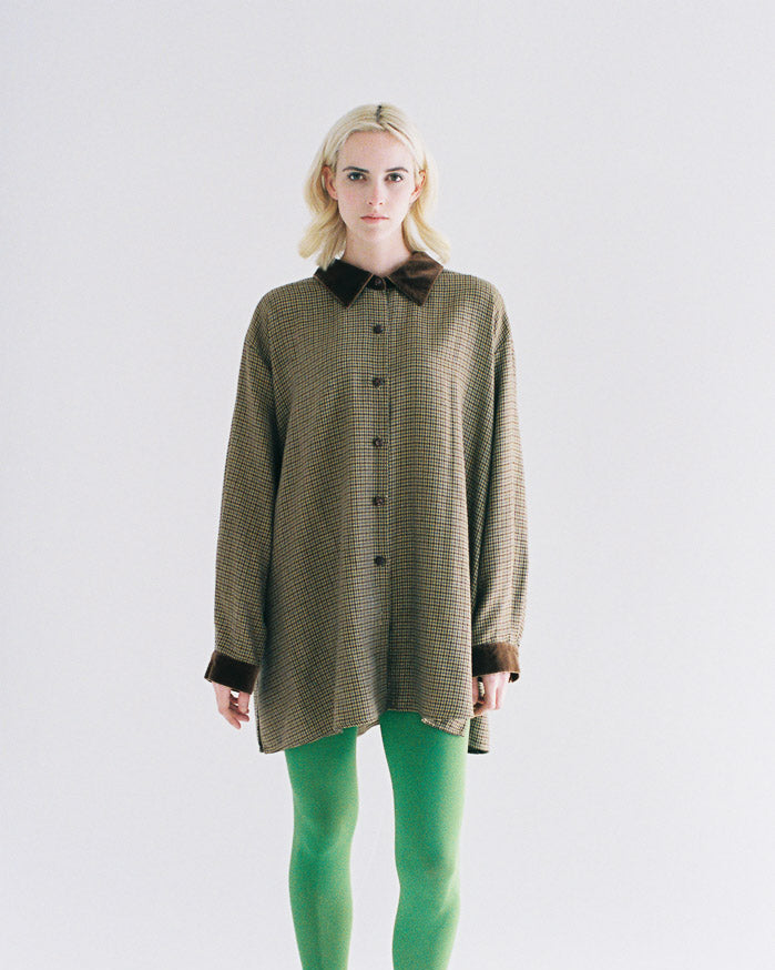 Person wearing a long brown checkered shirt with a black collar on a white background