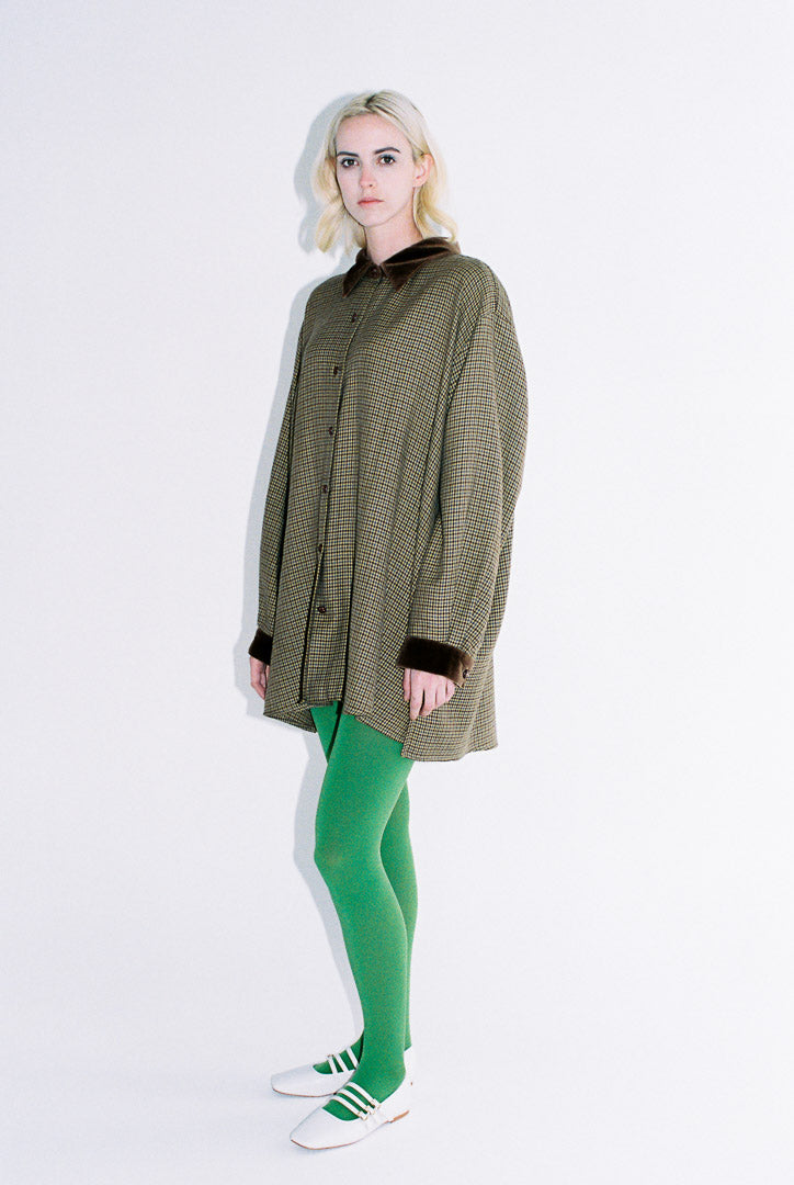Woman wearing a long coat, green leggings, and white sneakers on a white background