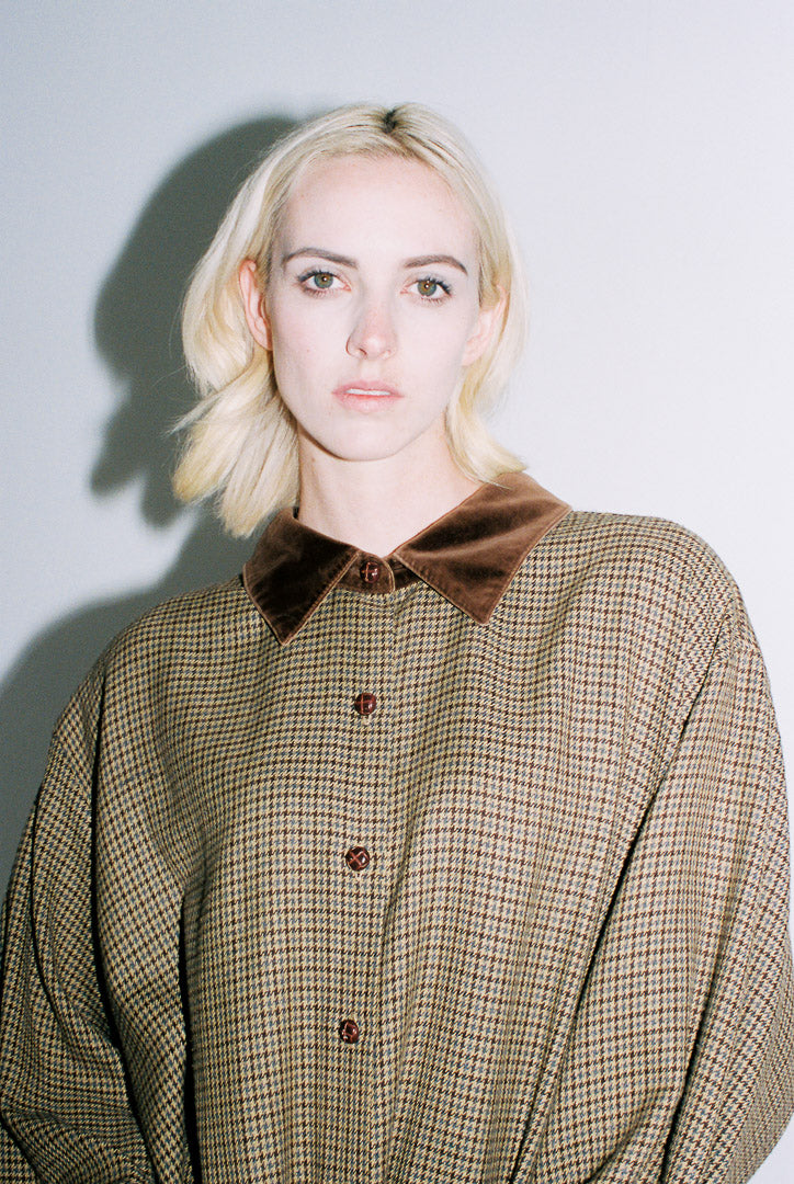 Woman wearing a plaid shirt with a brown collar against a plain background