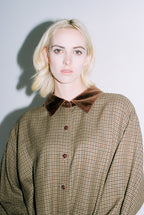 Woman wearing a plaid shirt with a brown collar against a plain background