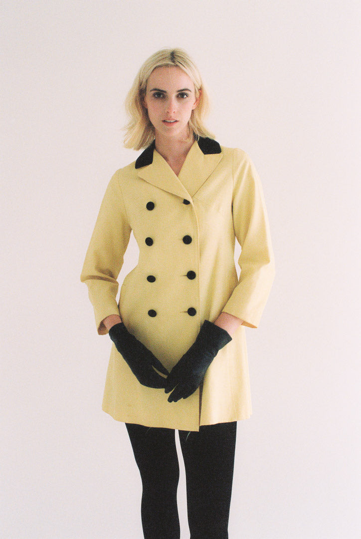 Woman wearing a yellow coat with black buttons and gloves on a white background