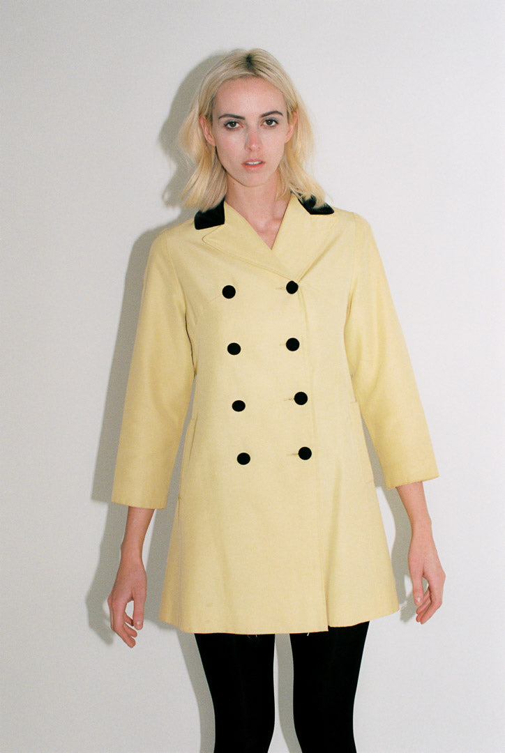 Woman wearing a yellow coat with black buttons against a white background