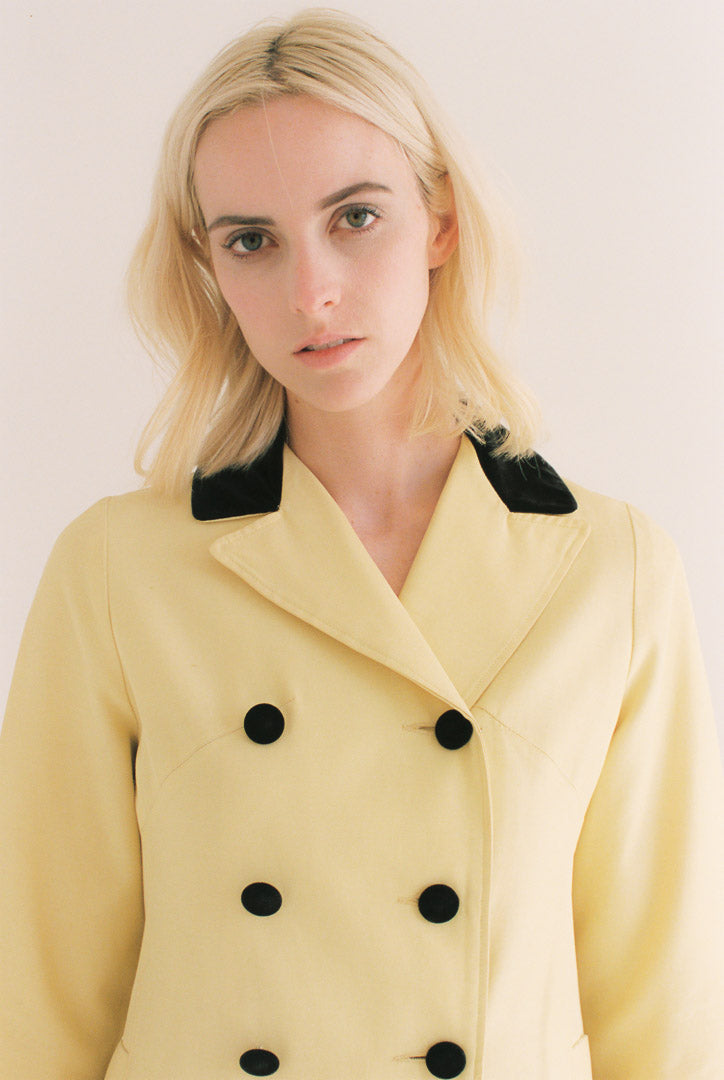 Woman wearing a yellow coat with black buttons against a plain background