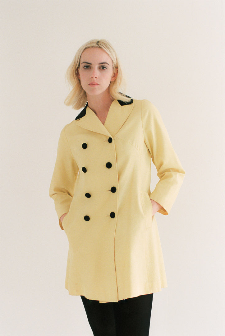 Woman wearing a yellow coat with black buttons on a plain background