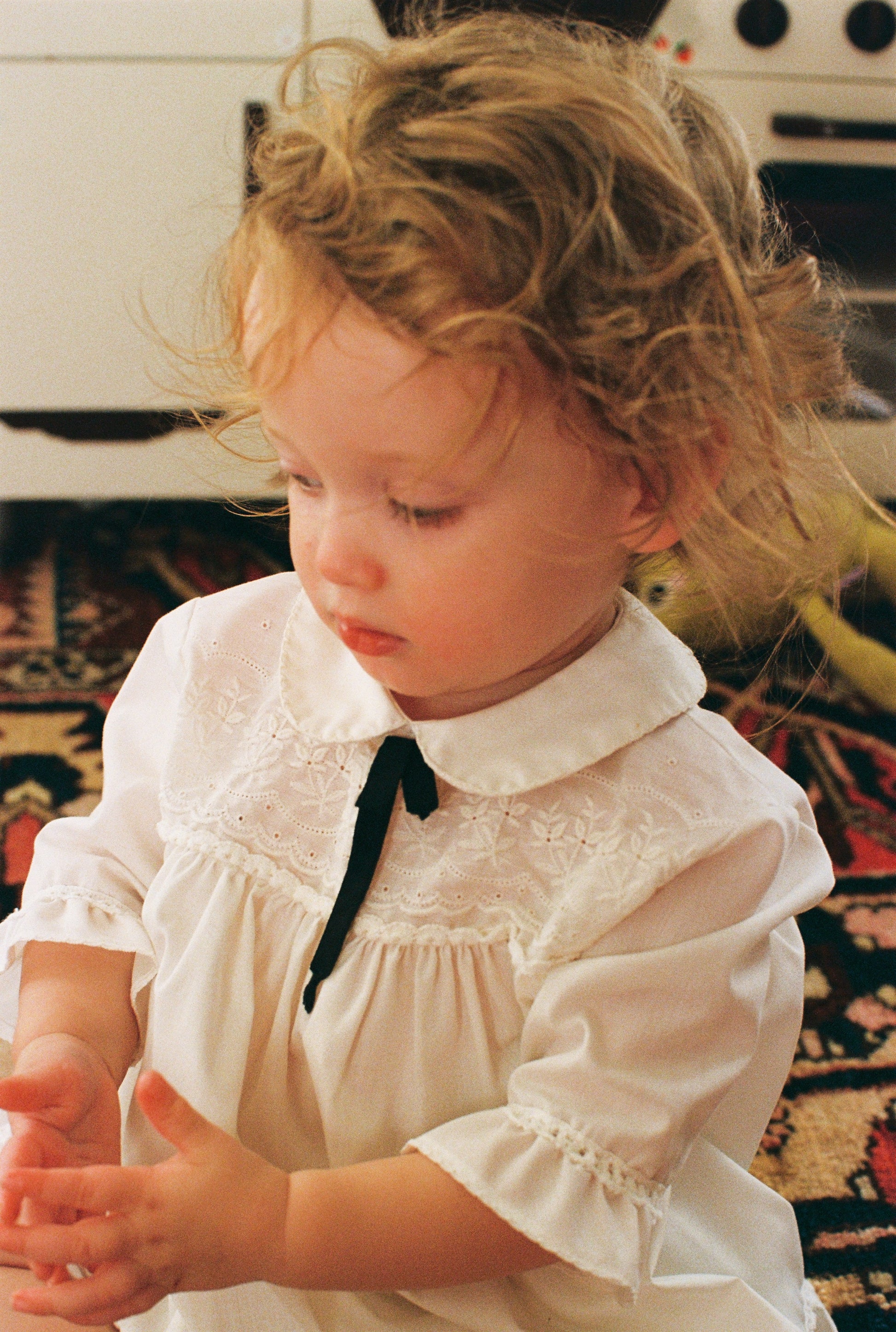 Child wearing a vintage white dress with a black bow in a home setting