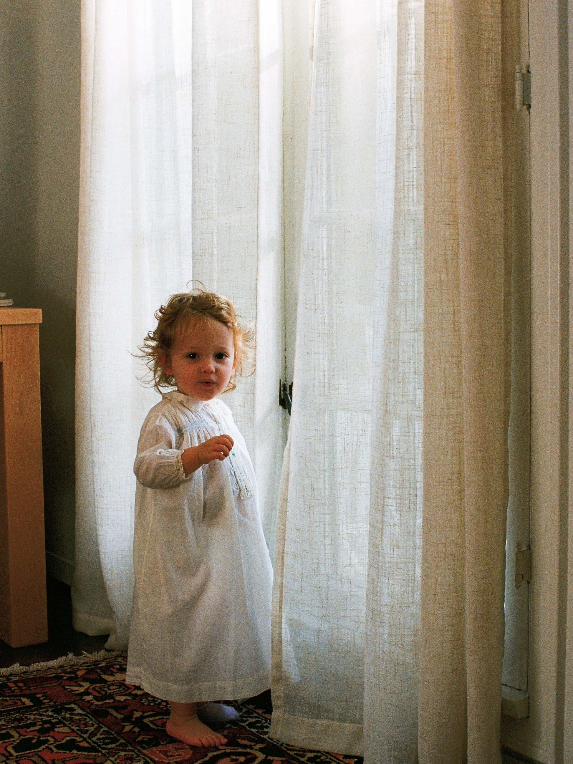 Child in a white dress standing behind sheer curtains