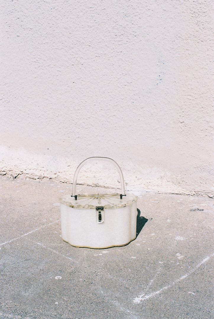 White bucket with a handle on a concrete surface against a light brick wall.