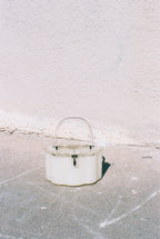 White bucket with a handle on a concrete surface against a light brick wall.