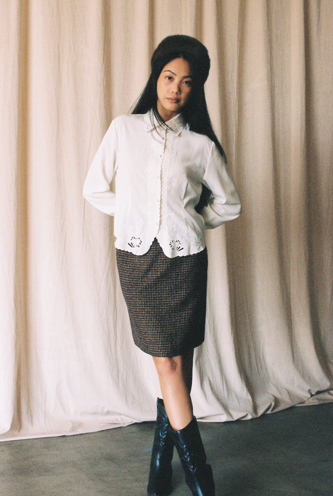 Woman wearing a white blouse with lace details and a black skirt against a beige curtain.