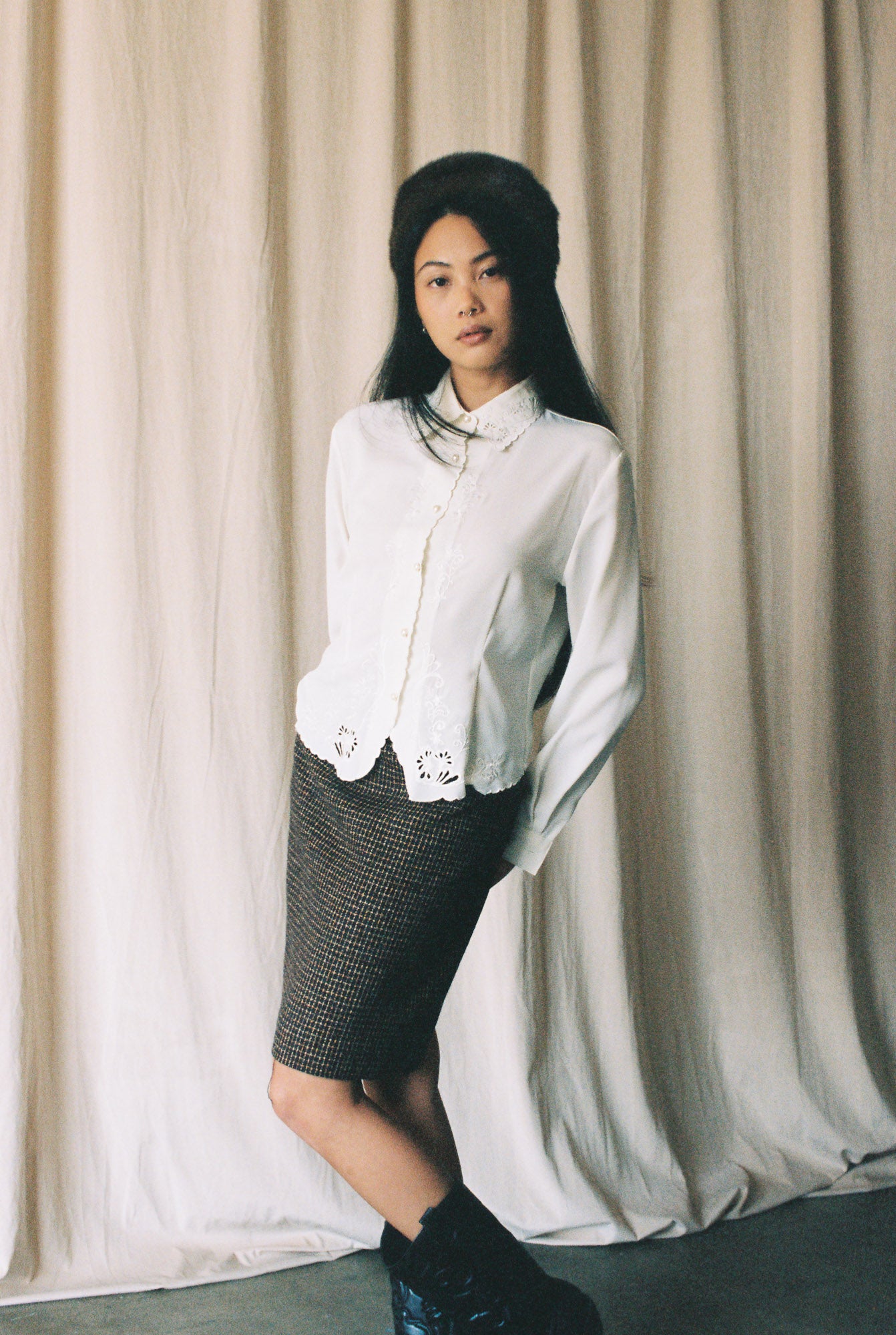 Woman wearing a white blouse and black skirt standing against a beige curtain.