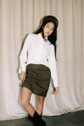 Woman wearing a white blouse and patterned skirt against a plain background