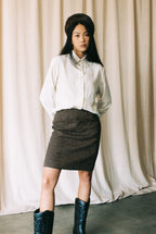 Woman wearing a white blouse, patterned skirt, and black boots against a plain background