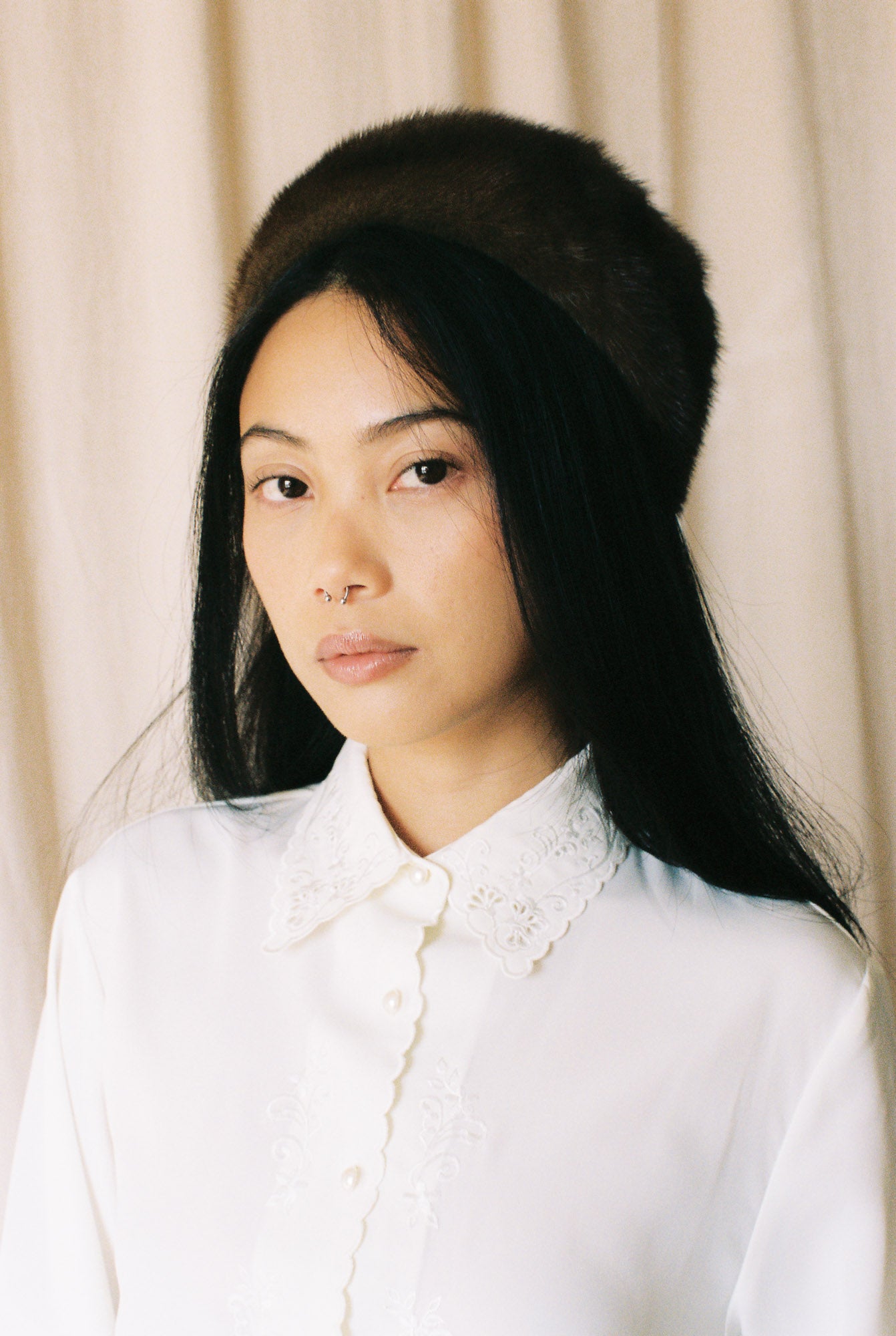 Woman wearing a white blouse with a beige curtain background