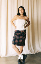 Woman wearing a white top and plaid skirt against a beige curtain background