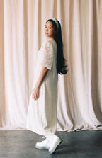 Woman in a white dress standing against a beige curtain