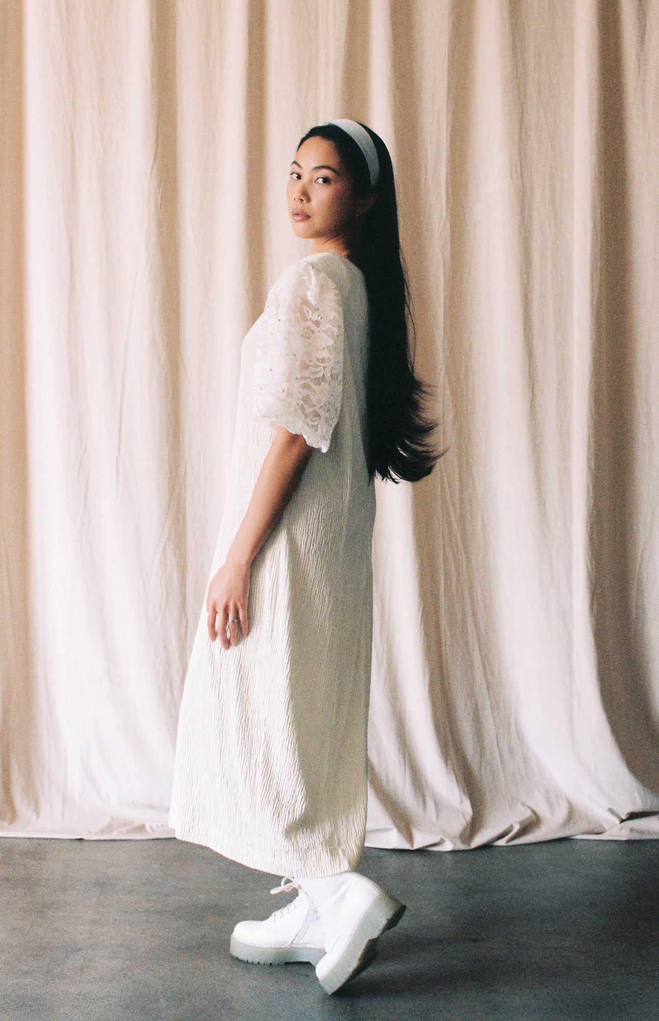 Woman in a white dress standing against a beige curtain