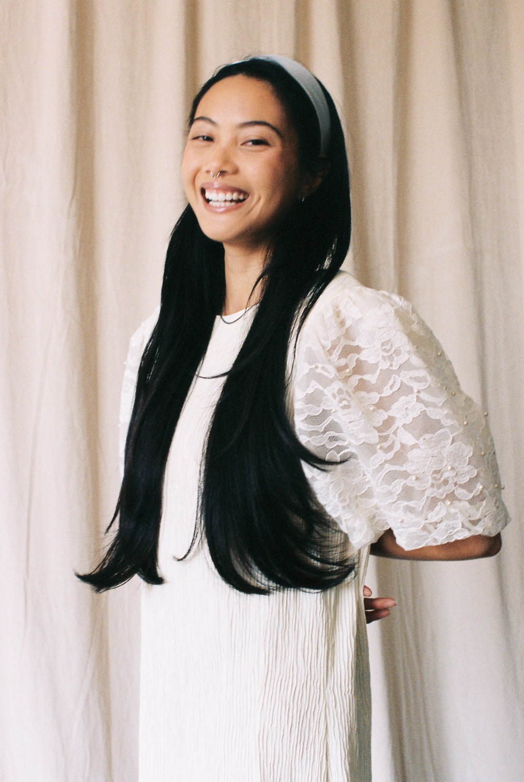 Woman wearing a white dress with lace sleeves against a beige curtain background