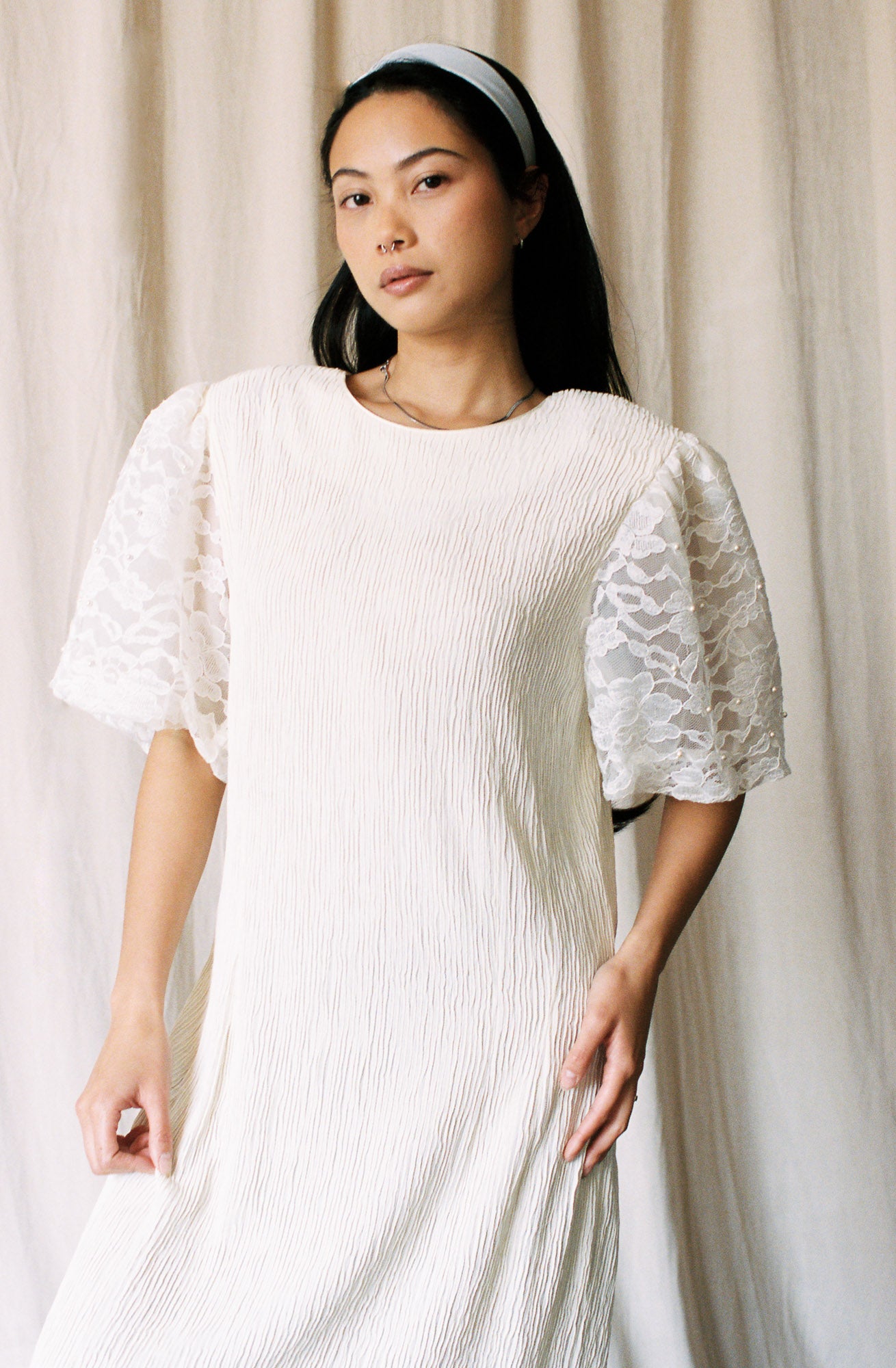 Woman wearing a white dress with lace sleeves against a beige curtain background
