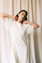 Woman wearing a white dress with lace sleeves against a beige curtain background
