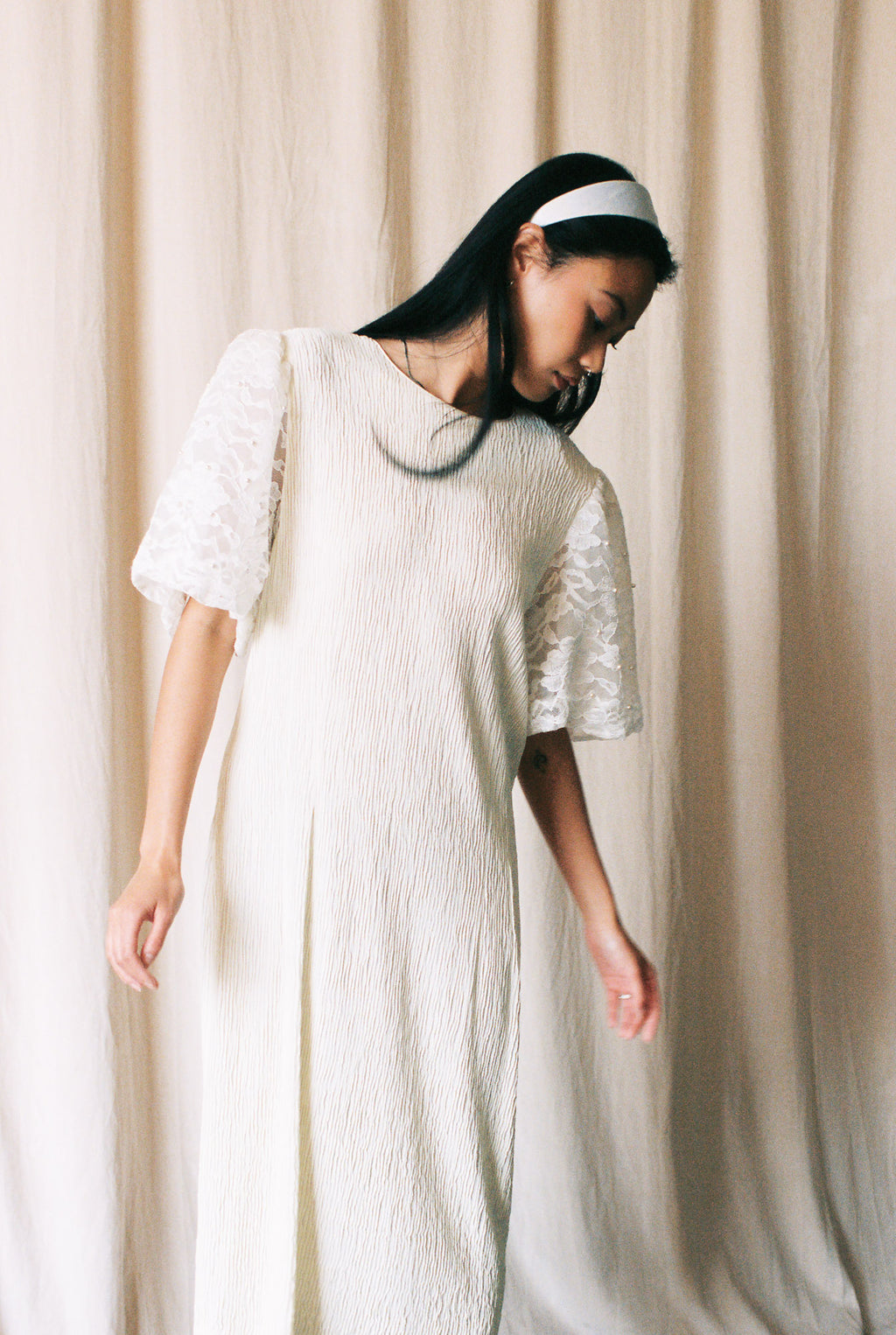 Woman wearing a white dress with lace sleeves against a beige curtain background