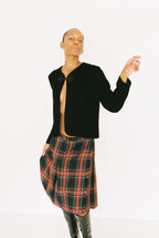 Person wearing a black jacket and plaid skirt on a white background