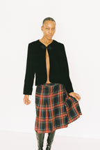 Person wearing a black jacket and plaid skirt on a white background