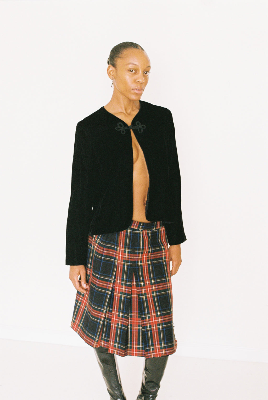Person wearing a black jacket and plaid skirt on a white background