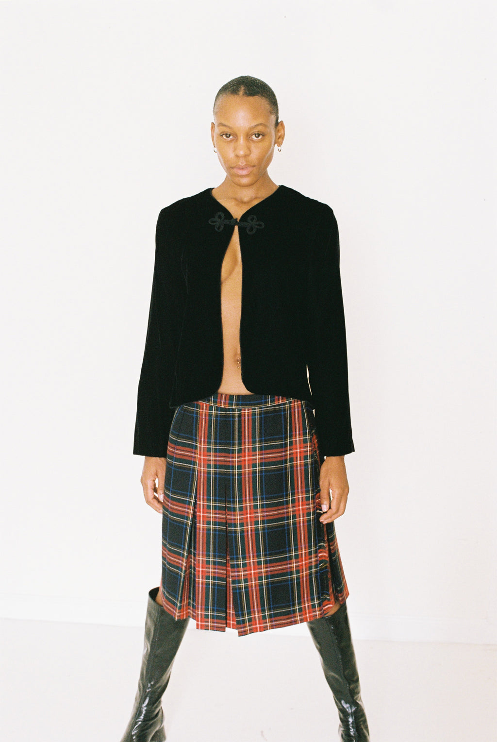 Person wearing a black blazer, plaid skirt, and black boots on a white background
