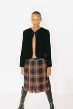 Person wearing a black blazer, plaid skirt, and black boots on a white background