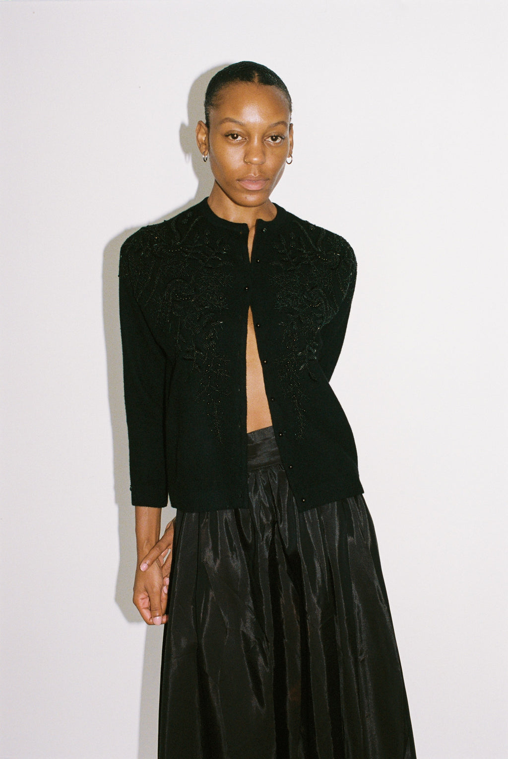 Person wearing a black outfit with a textured top and flowing pants on a white background