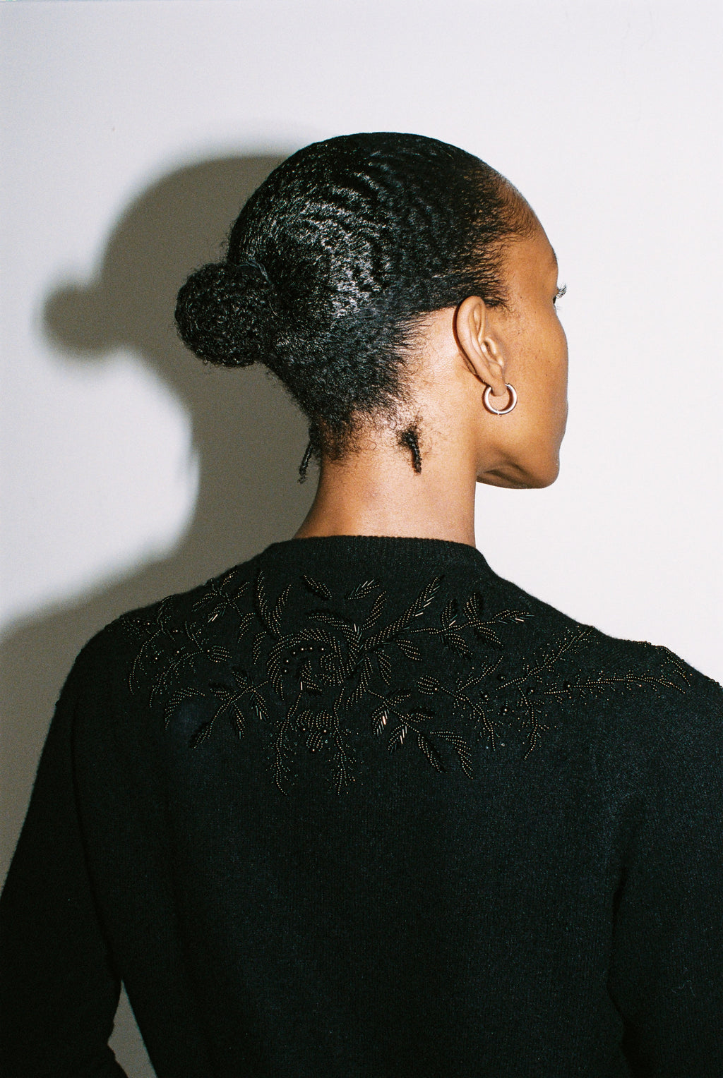 Person wearing a black sweater with intricate detailing on the back against a white background