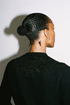 Person wearing a black sweater with intricate detailing on the back against a white background