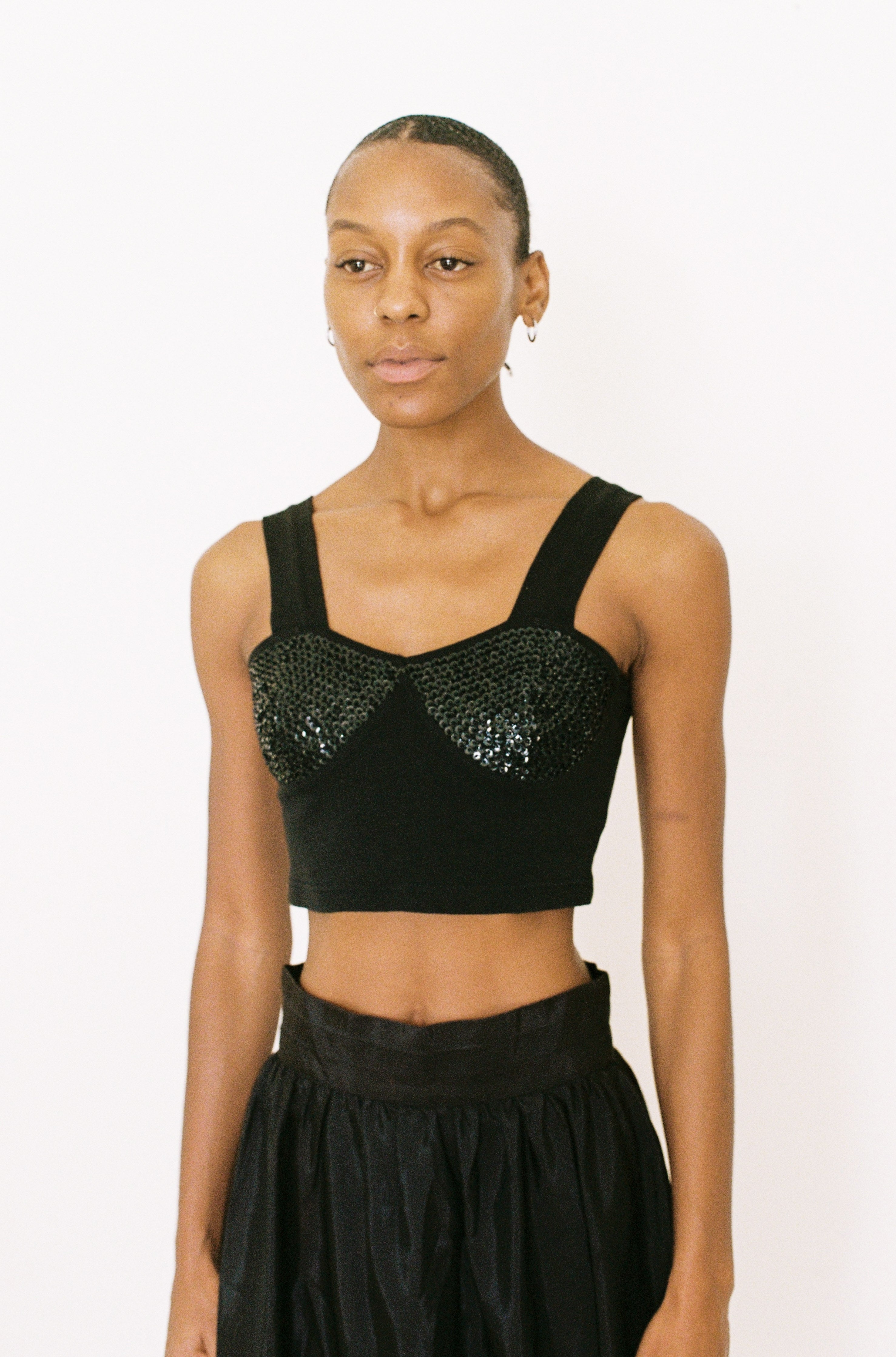 Woman wearing a black crop top with sequin detailing on a white background