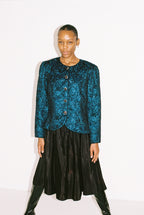 Person wearing a blue patterned jacket and black skirt on a white background