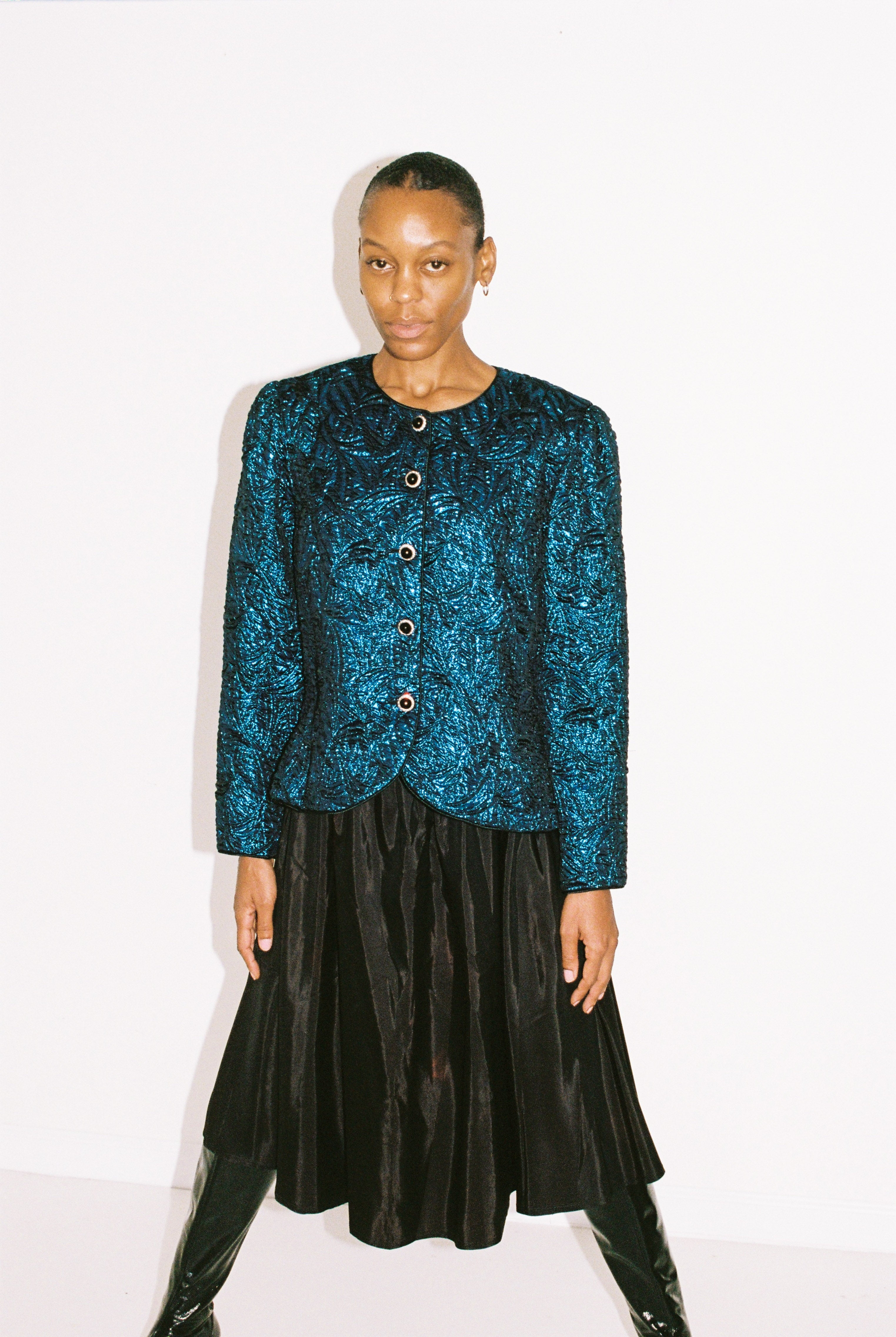 Person wearing a blue patterned jacket and black skirt on a white background