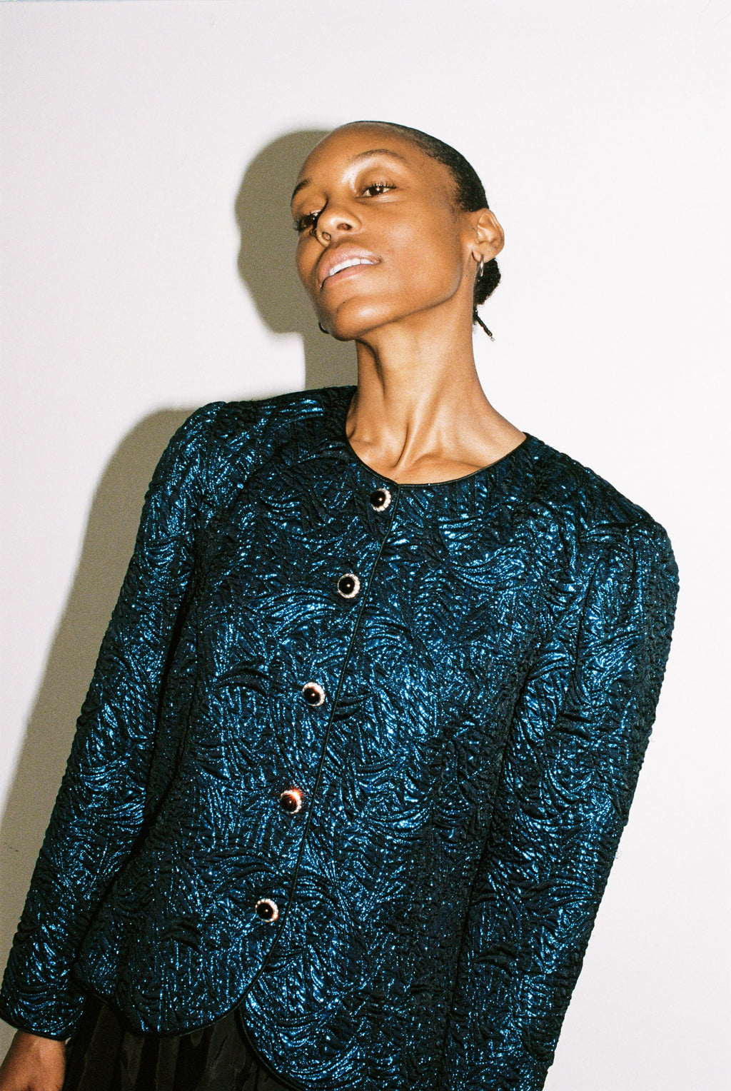 Woman wearing a textured blue jacket with buttons on a plain background