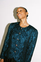 Woman wearing a textured blue jacket with buttons on a plain background