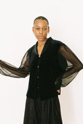 Person wearing a black outfit with sheer sleeves against a white background