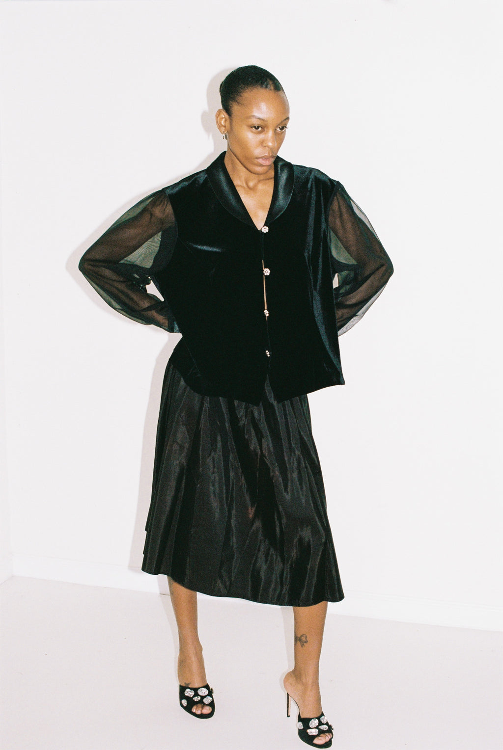 Person wearing a black outfit with sheer sleeves on a white background