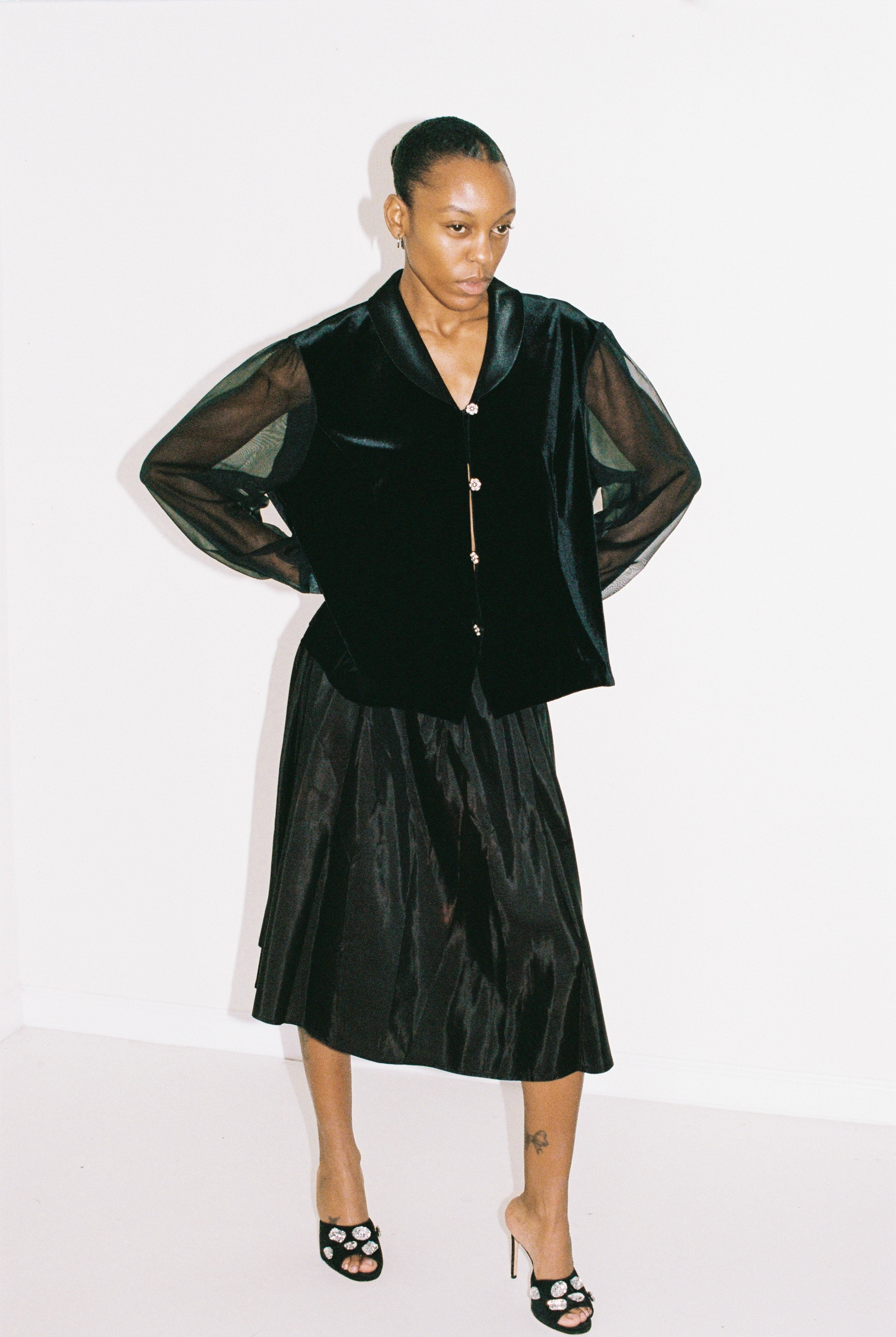 Person wearing a black outfit with sheer sleeves on a white background