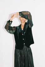 Person wearing a black velvet outfit with sheer sleeves against a white background