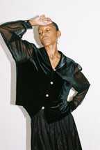 Person wearing a black satin outfit with sheer sleeves on a white background