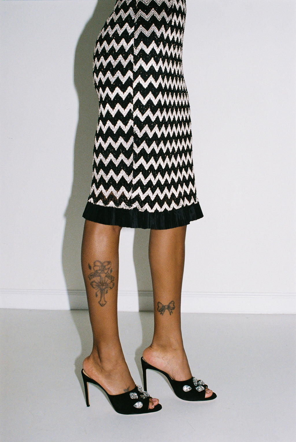 Person wearing a black and silver zigzag patterned skirt with high-heeled shoes on a plain background