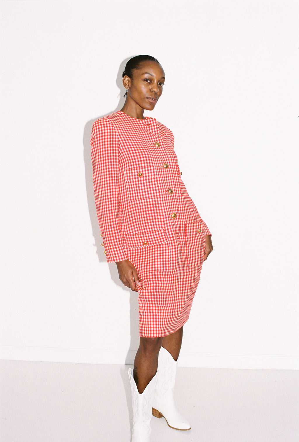 Woman wearing a red and white checkered dress with white boots on a white background