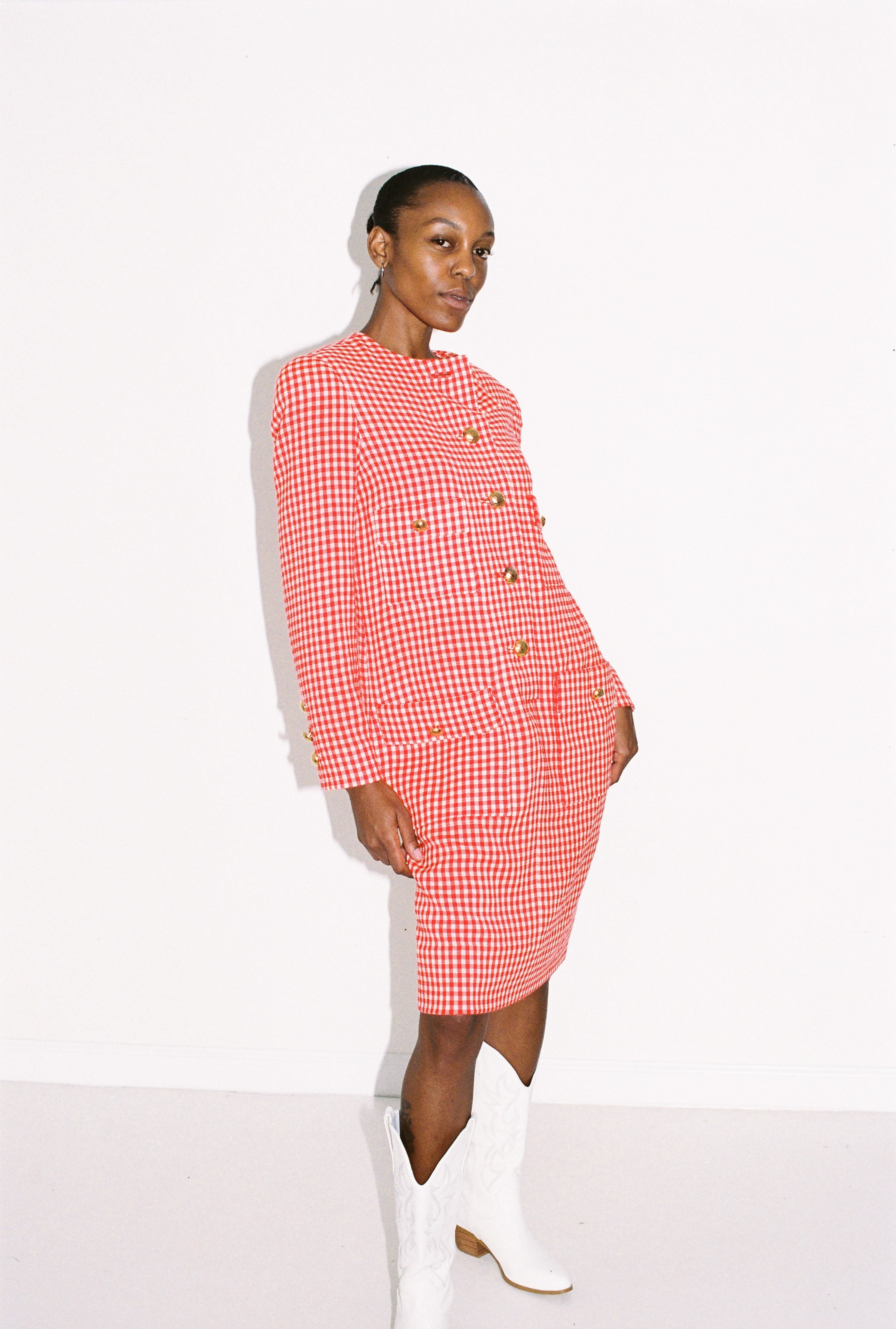 Woman wearing a red and white checkered dress with white boots on a white background