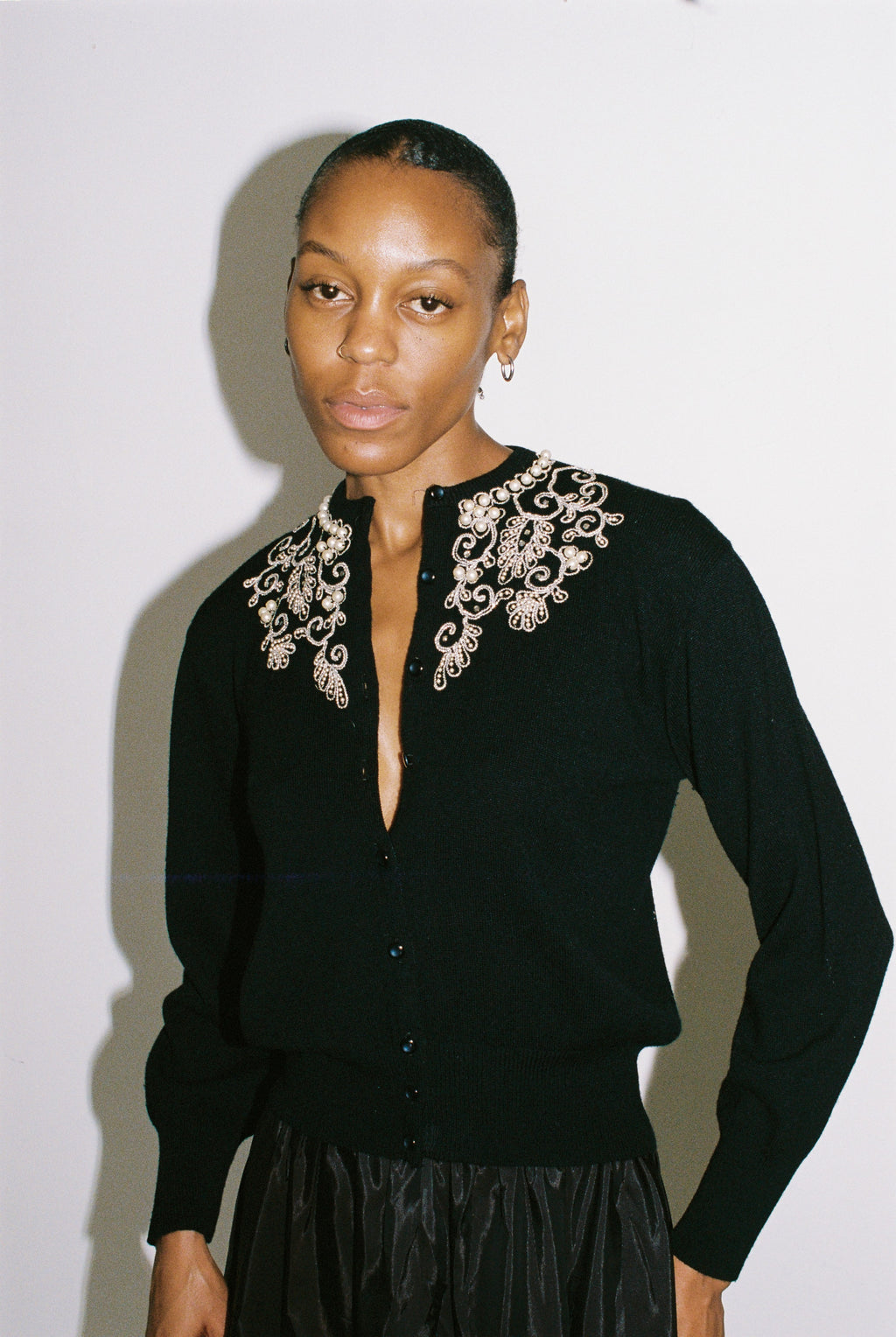 Woman wearing a black cardigan with intricate silver embroidery on a plain background