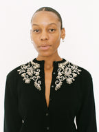 Woman wearing a black outfit with an ornate white collar against a white background