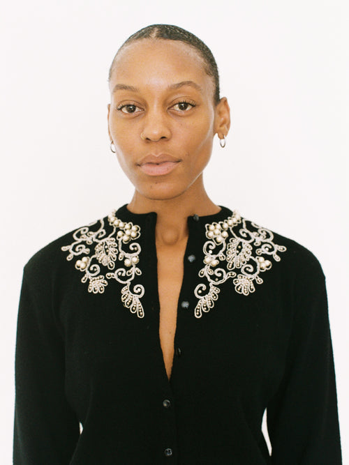 Woman wearing a black outfit with an ornate white collar against a white background